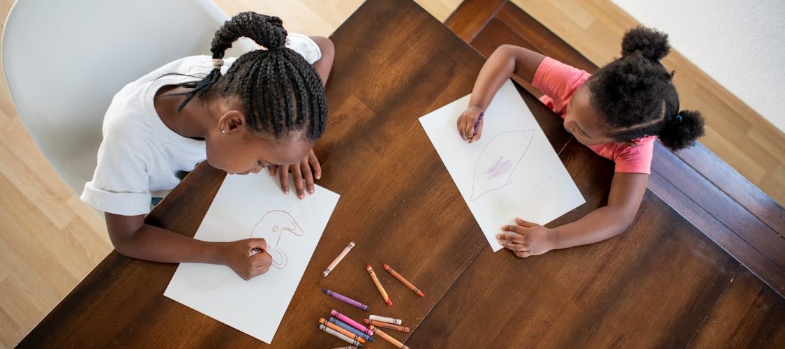 Two young African American girls sit at a table and make art.