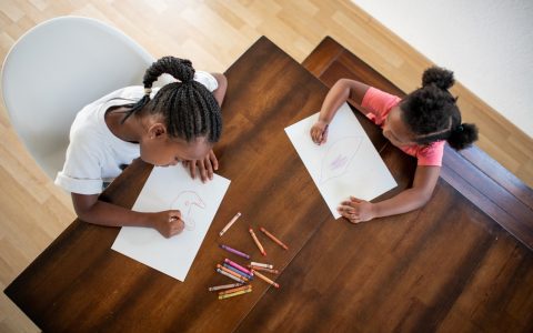 Two young African American girls sit at a table and make art.