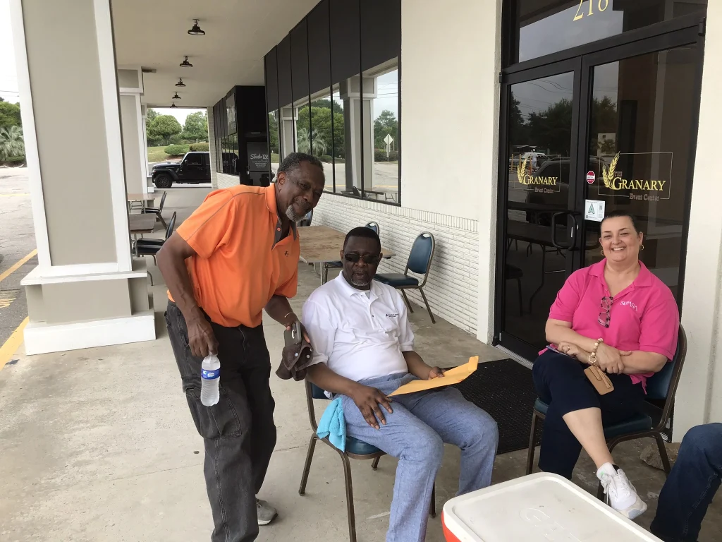 Members of the community at a car show. The picture shows a two men and a woman.