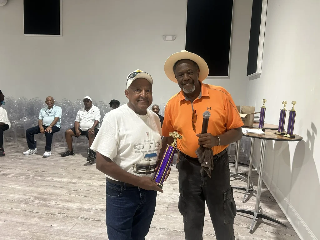 A man in an orange shirt passes out an award at the classic car show
