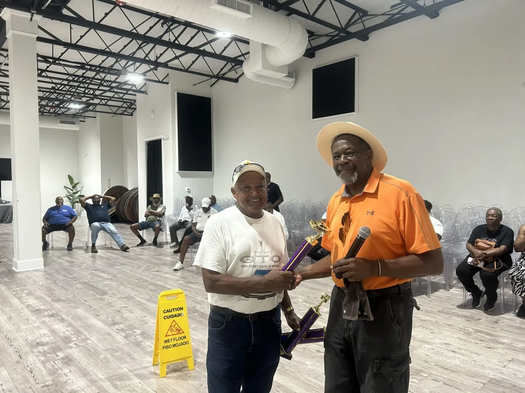 A man in an orange shirt passes out an award at the classic car show